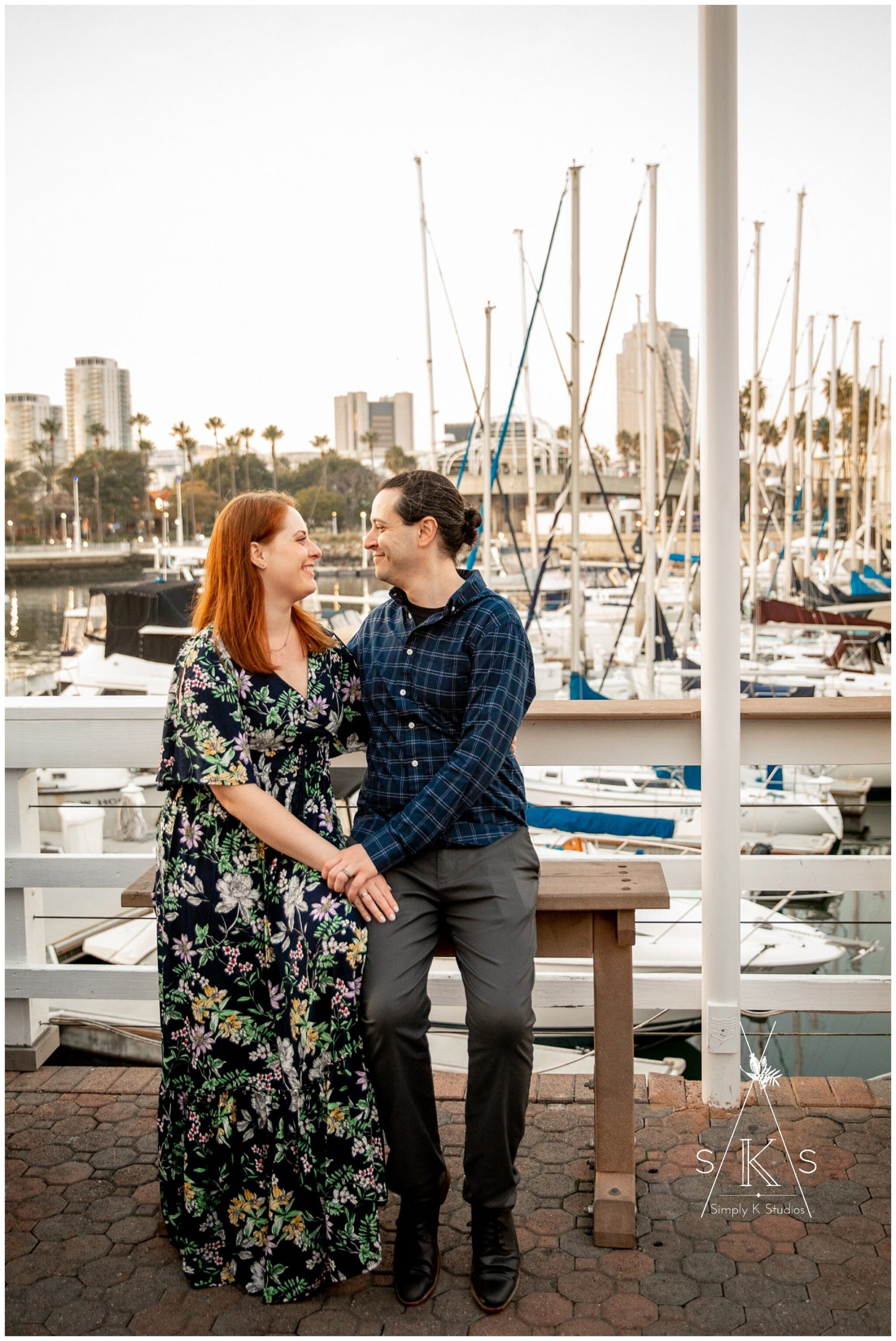  Engaged couple sitting on a bench with sailboats in the background 