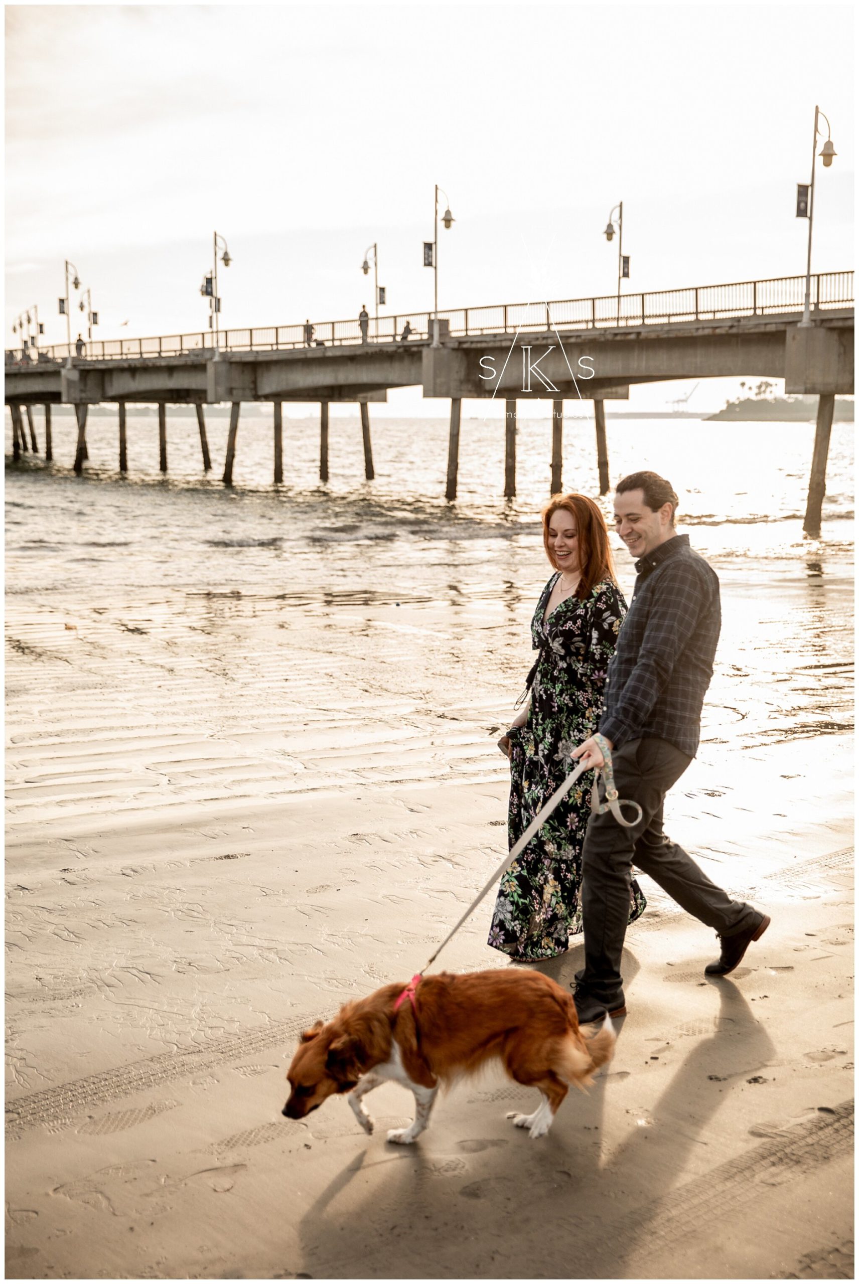  Man and woman walking their dog on the beach in front of a pier 