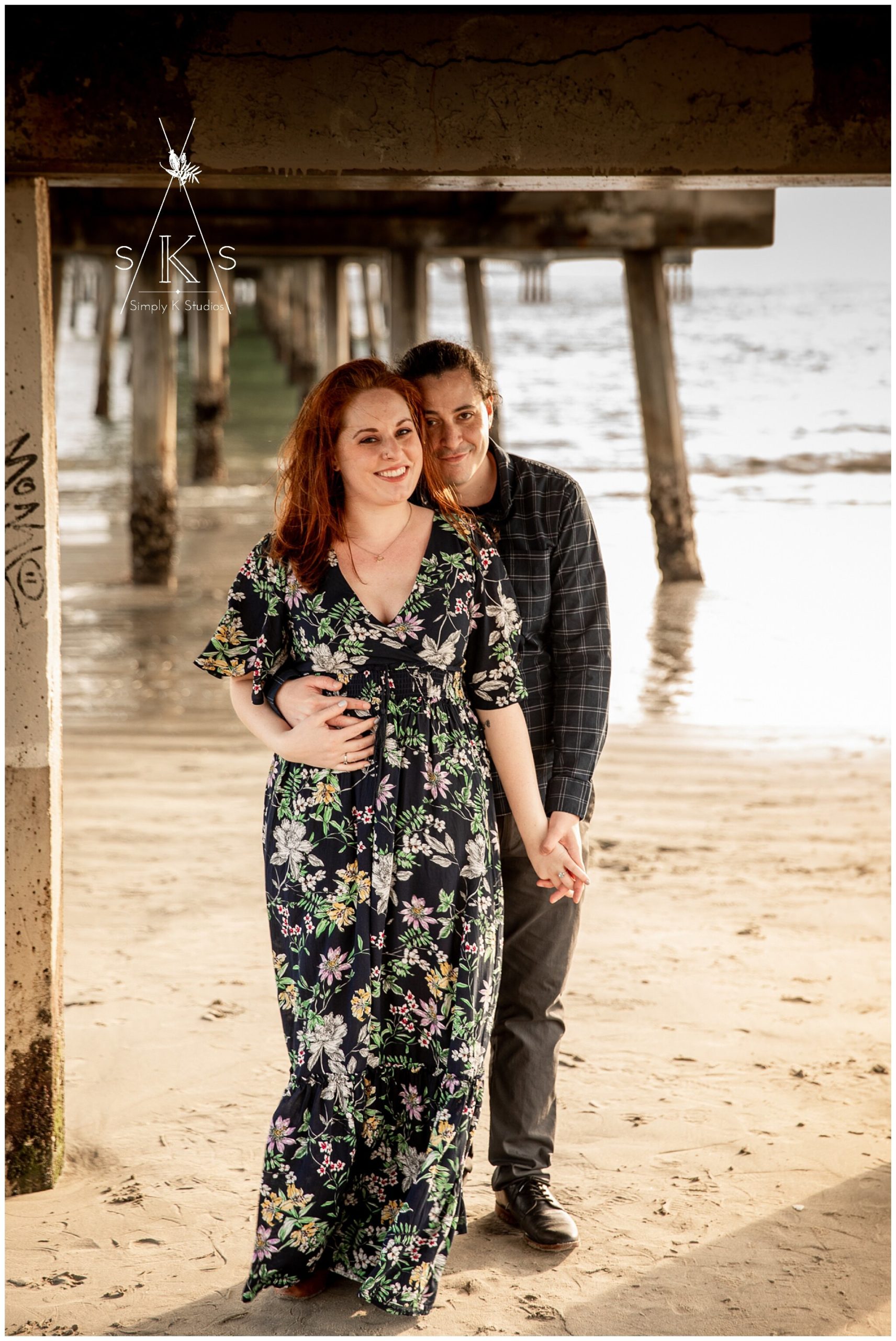  A man and woman holding hands underneath a pier on the beach 
